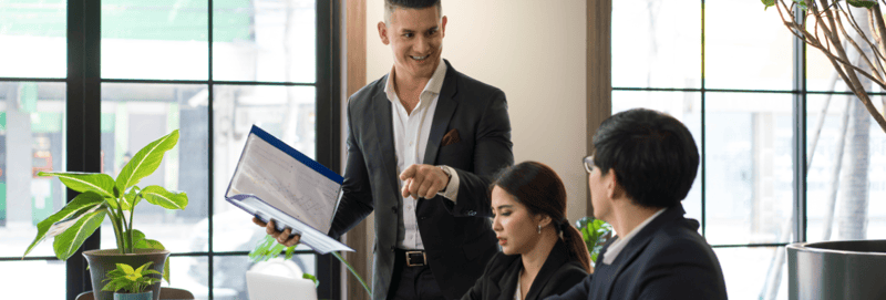 Sales manager talking to two sales people while holding a laptop on his hand