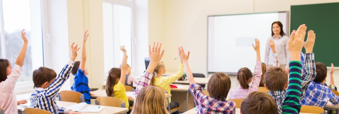 Children raising their hand in a classroom while teacher asks question
