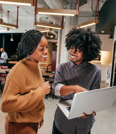 A woman and a man standing up holding a laptop and smiling