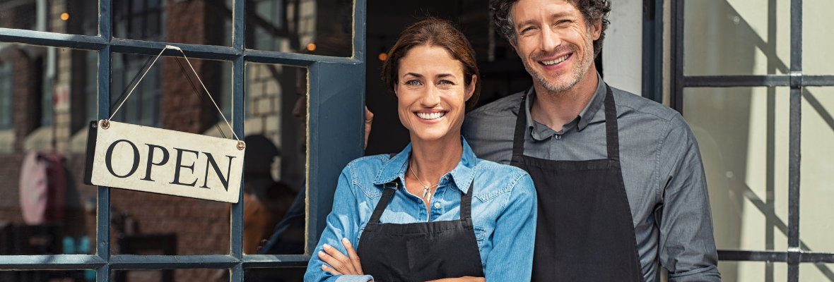 Two business owners standing in front of their business with an open sign on the door