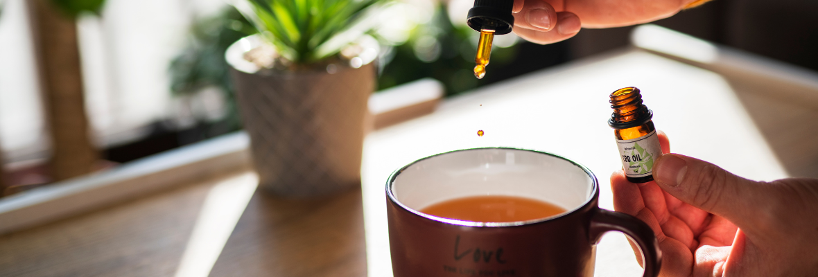 A hand putting drops of CBD oil into a cup