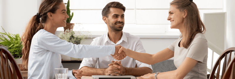 Three marketers sitting on a table, one smiling as the other two shake hands