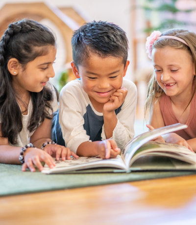 Three young children reading a book at school