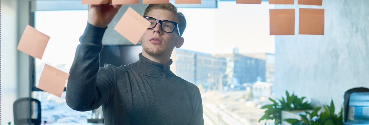 A young business man putting some post-it notes through a glass panel.