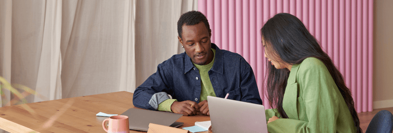 A male and female co-workers sitting on a table working on their laptop