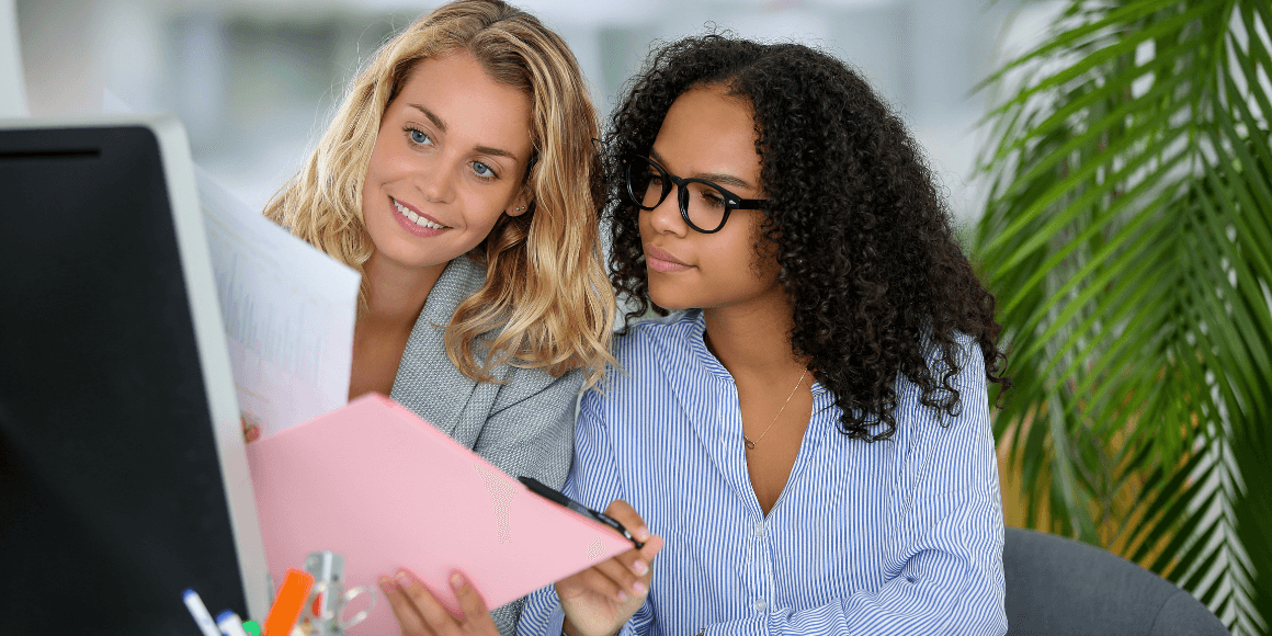 Two female marketers looking at a screen while holding some paperwork