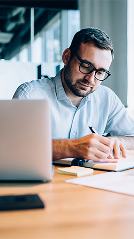 man taking notes on pad in front of his laptop